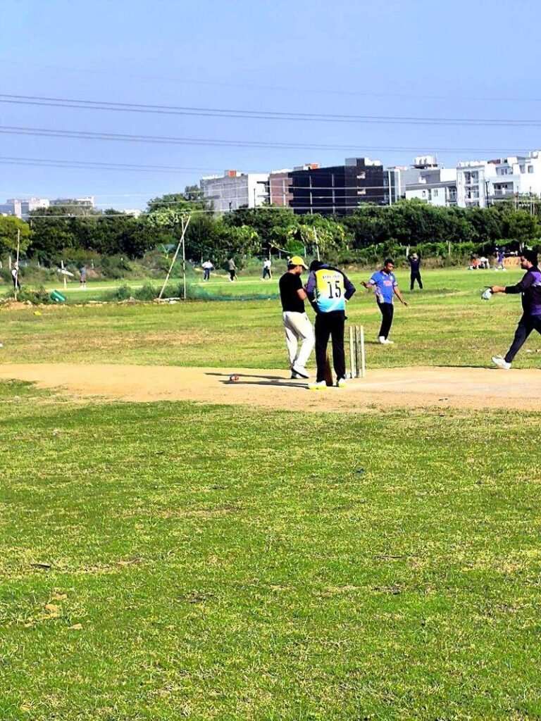 Players between deliveries on a dirt pitch during an amateur cricket match